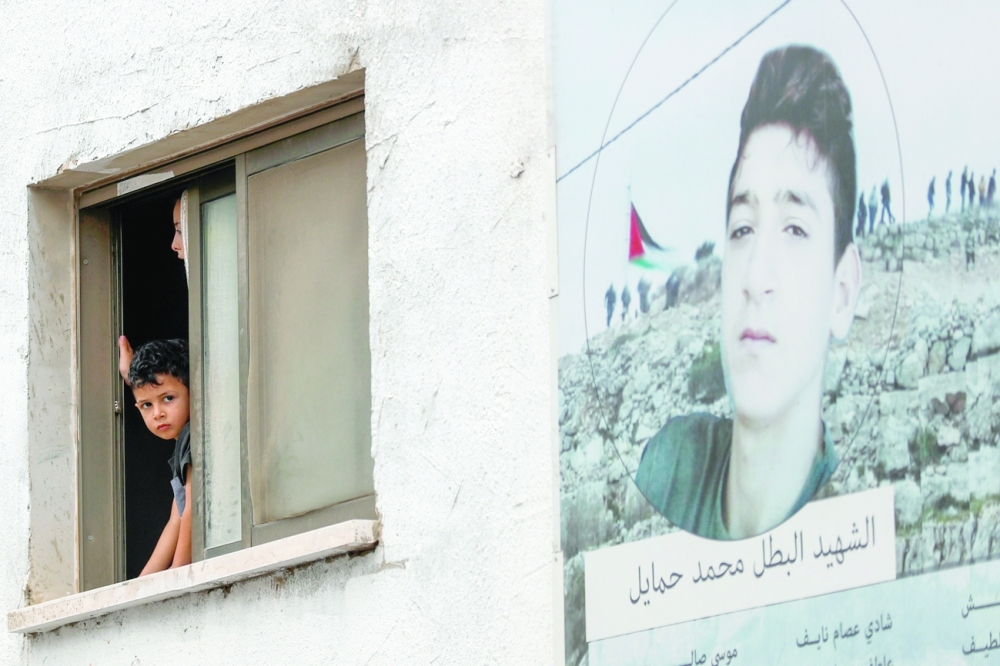  صبي يطل من النافذة بجوار ملصق للشهيد أحمد زاهي خلال التشييع في بيتا بالضفة  "رويترز"