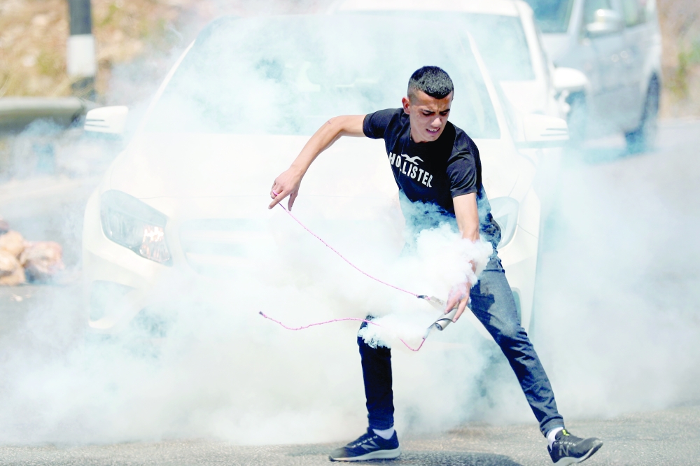 متظاهر فلسطيني يستعد للتخلص من قنبلة غاز مسيل للدموع أطلقتها القوات الإسرائيلية خلال احتجاجات بالضفة الغربية أمس.رويترز