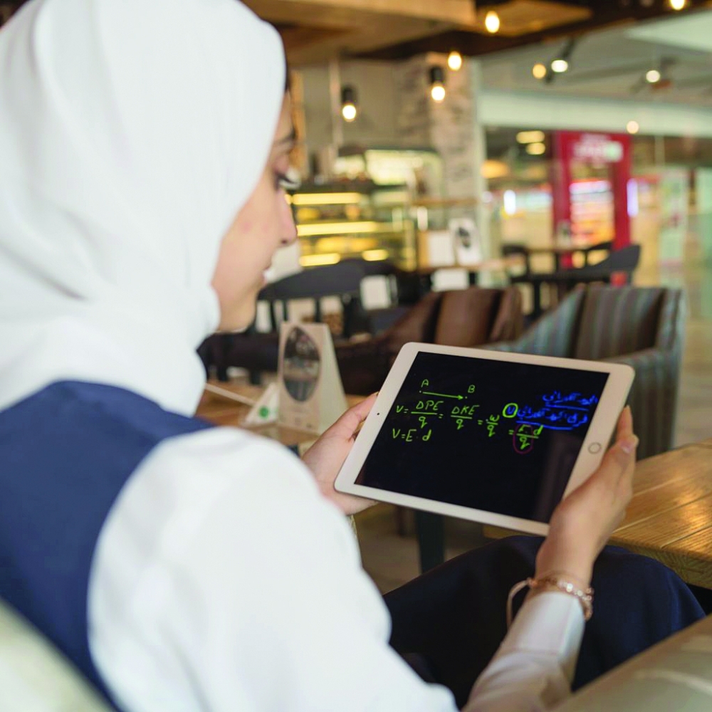 طالبة تمسك بجهازها اللوحي للاطلاع على الحصة الدراسية خلال فترة التعلم عن بعد