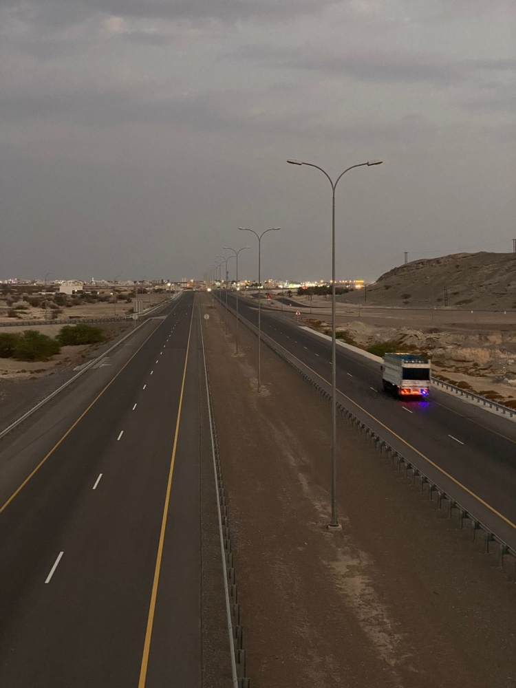 صورة من فوق الجسر تظهر مرور أحد المركبات الثقيلة على طريق أدم وقت الغروب