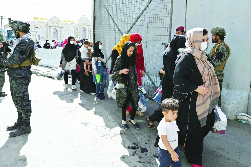 مقاتلو طالبان  يقفون باعمال الحراسة بينما يسير  مجموعة من الاسر الافغانية التي تامل مغادرة البلاد في اقرب وقت ممكن