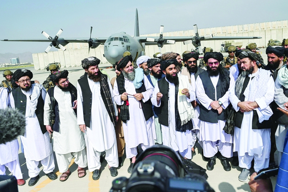 لمتحدث باسم طالبان ذبيح الله مجاهد (وسط ، يرتدي شال) يتحدث إلى وسائل الإعلام في مطار كابول أمس بعد مغادرة القوات الأمريكية افغانستان.أ.ف.ب 