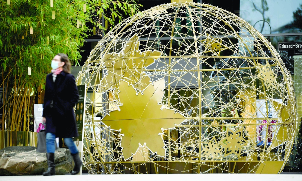 امرأة ترتدي قناعًا لحماية الوجه تسير بجوار زينة عيد الميلاد لمركز تسوق في شتوتغارت أمس بجنوب ألمانيا.أ.ف.ب