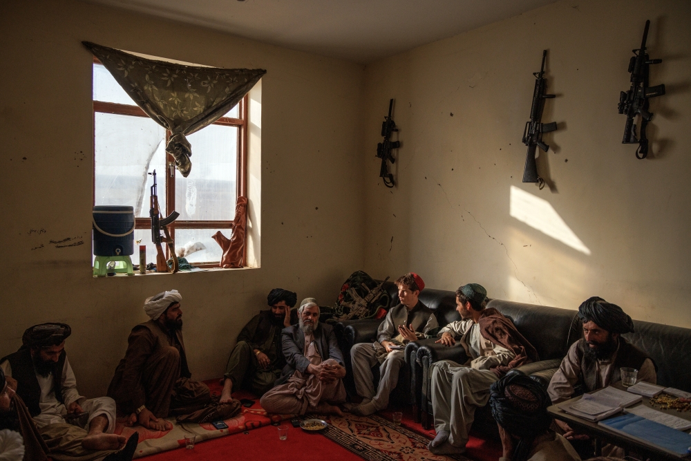 New York Times reporter Thomas Gibbons-Neff, third from right in red hat, interviews Mullah Abdul Rahim Gulab, sitting below the weapon in the window, in Marjah, Afghanistan, on Nov. 8, 2021. (Jim Huylebroek/The New York Times)