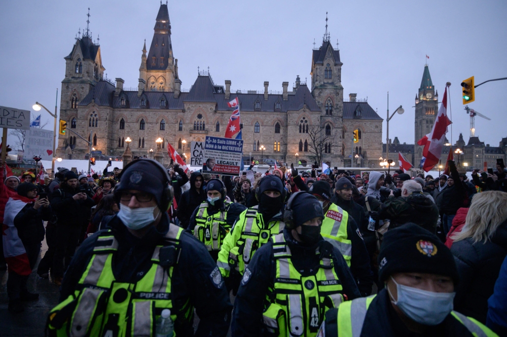 ضباط الشرطة يواجهون المتظاهرين أثناء احتجاج سائقي الشاحنات على قواعد الصحة الوبائية خارج البرلمان الكندي في أوتاوا أمس الأول.  (أ ف ب)
