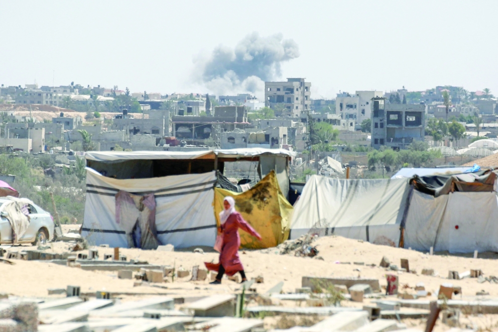 يتصاعد الدخان الناجم عن القصف الإسرائيلي في الخلفية بينما تمشي امرأة في خان يونس بجنوب قطاع غزة.  