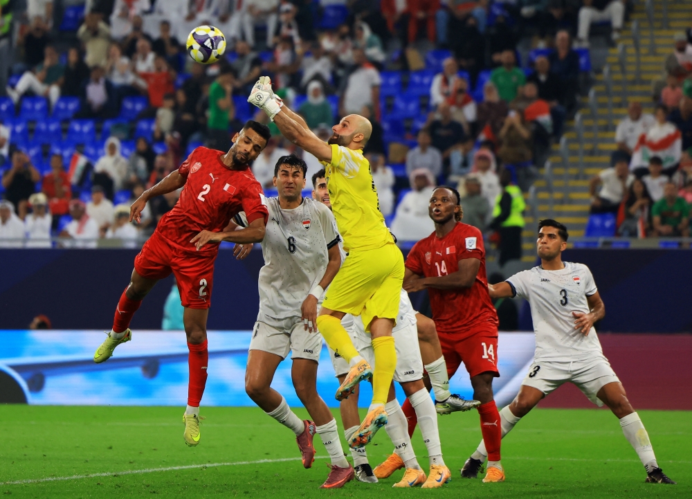 حارس منتخب العراق  أحمد باسل يبعد الكرة من أمام لاعب البحرين أمين بن عادي